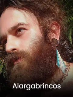 Modelo com barba e cabelo comprido usando alargador prateado com brinco pendente colorido, representando a categoria alargabrincos da Alargs.com.br